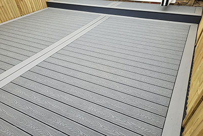 Grey composite decking with step in courtyard style back garden.