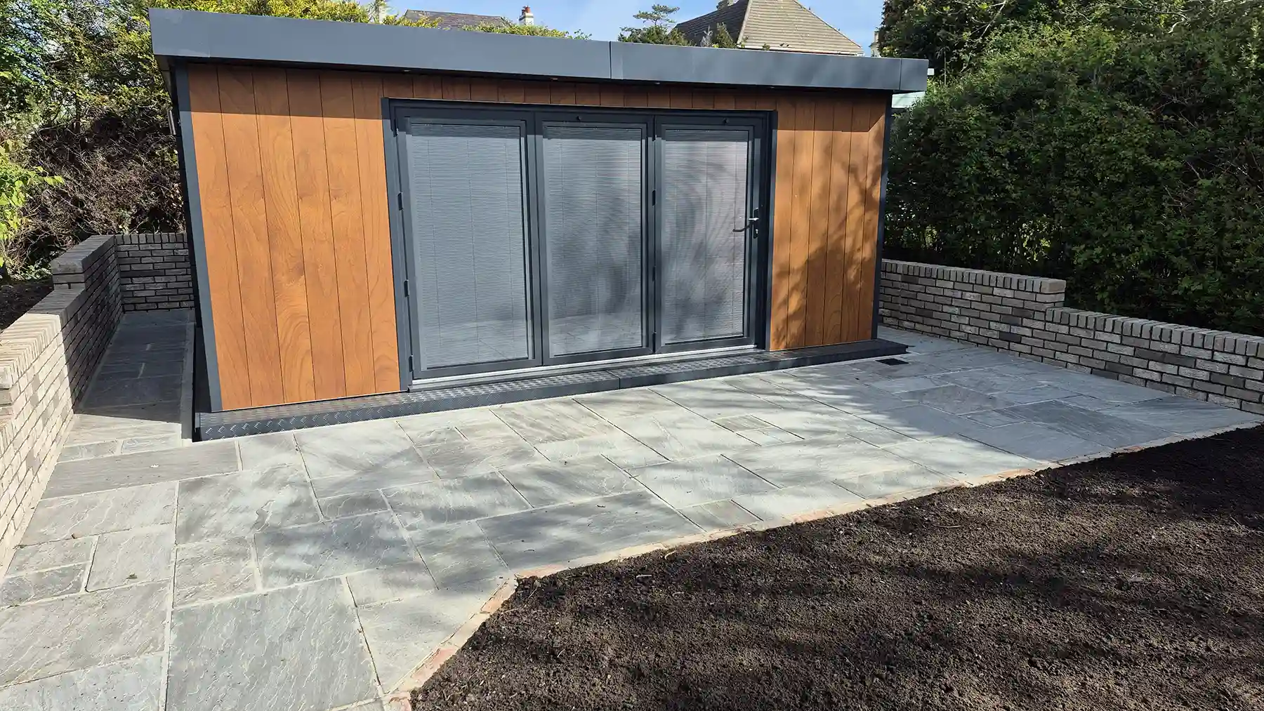 New garden building with a grey retaining wall and sandstone patio.
