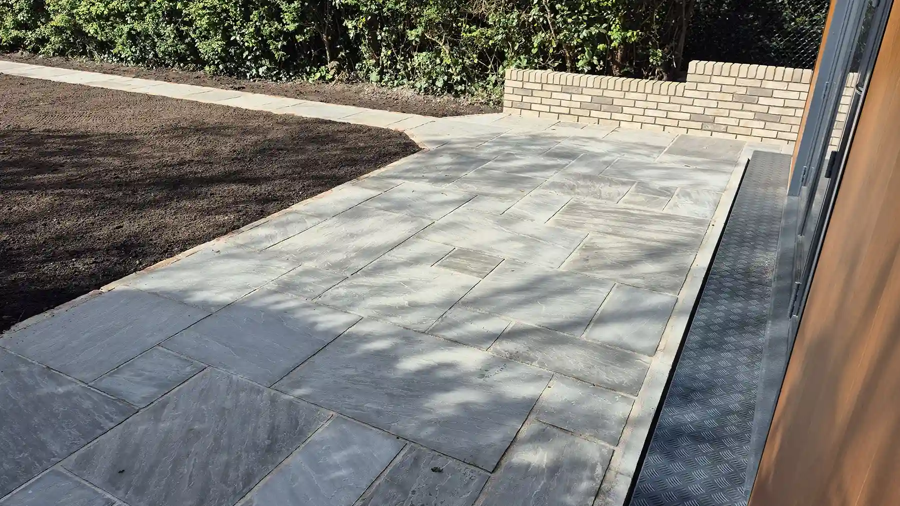 Grey sandstone patio with brick edging in front of a new garden building.
