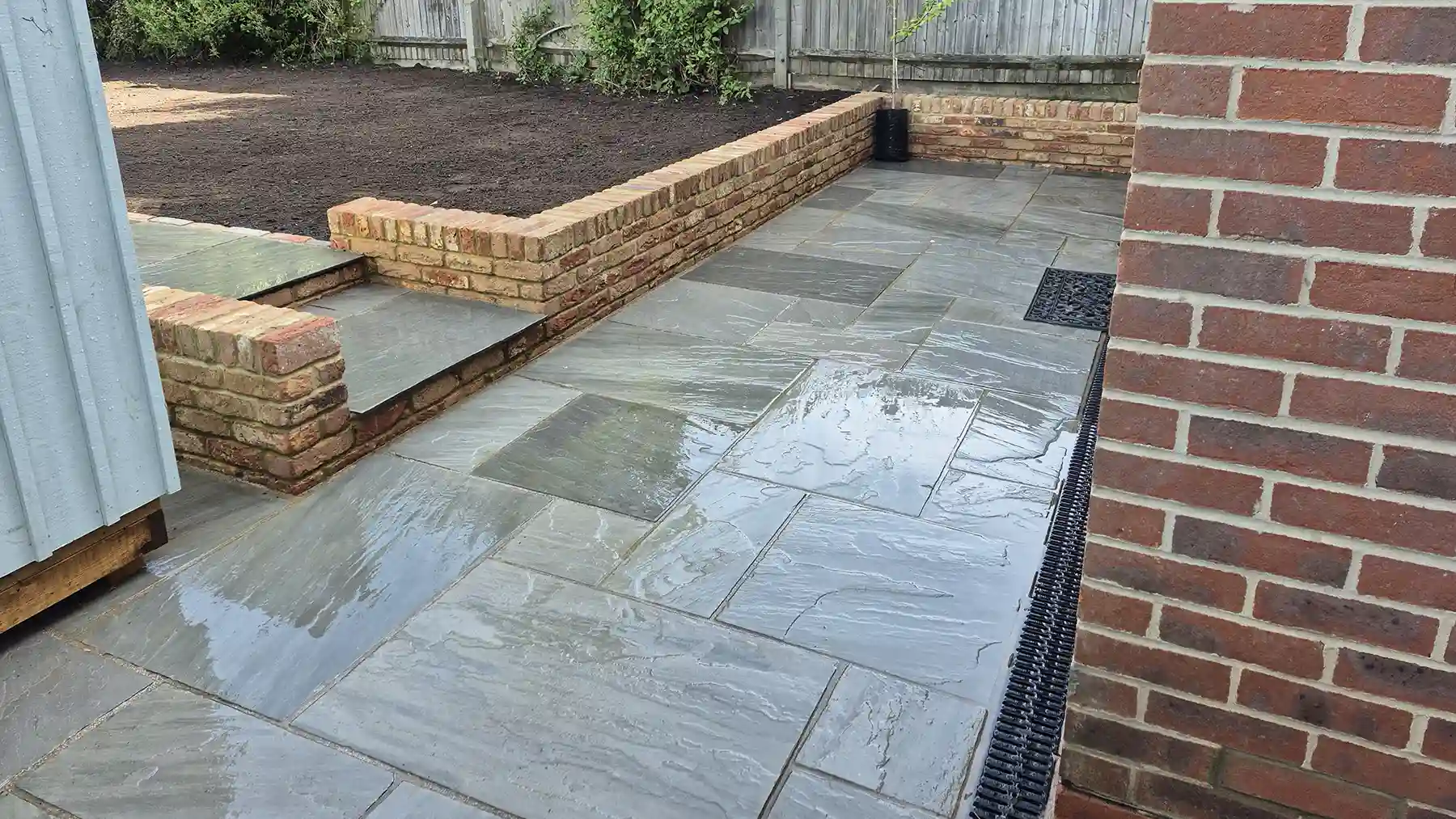 Grey sandstone patio with garden brick wall outside of patio doors.