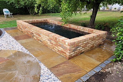 Old farmhouse brick build raised pond with water fountain in a cottage garden.
