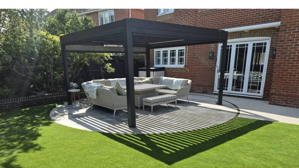 Artificial grass area with a large circulate porcelain patio with aluminium pergola with resin set around the house.