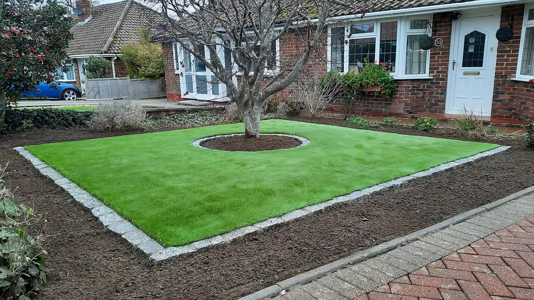 Artificial grass with granite edging with acre tree in the middle.