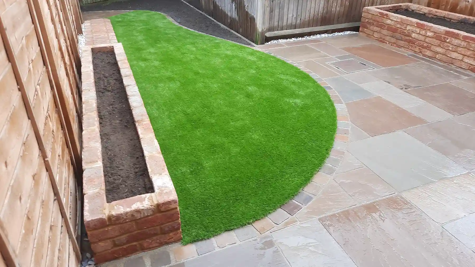 Old farmhouse raised brick flower beds set in a small back garden with patio and artificial grass.