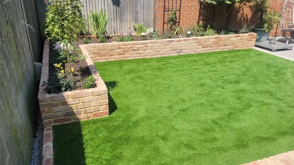 Raise brick build flower bed with old farmhouse bricks and artificial grass area.