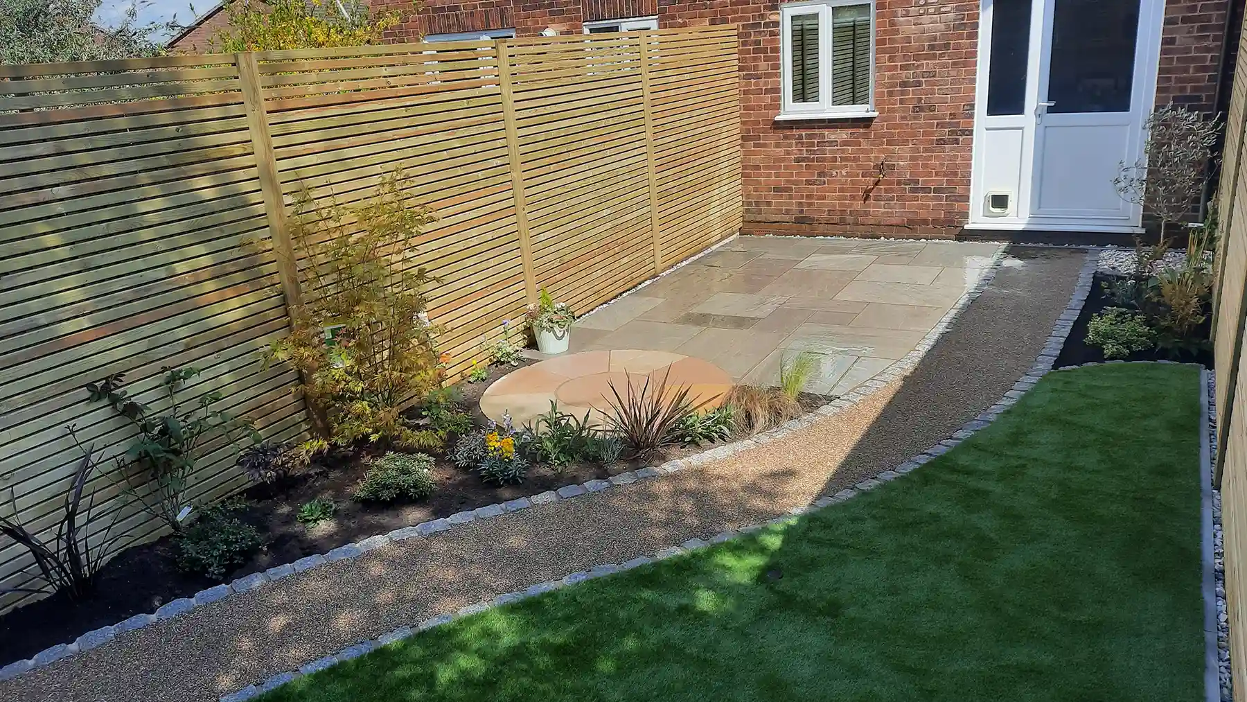 Small garden with sandstone patio, planting, resin path and artificial grass.