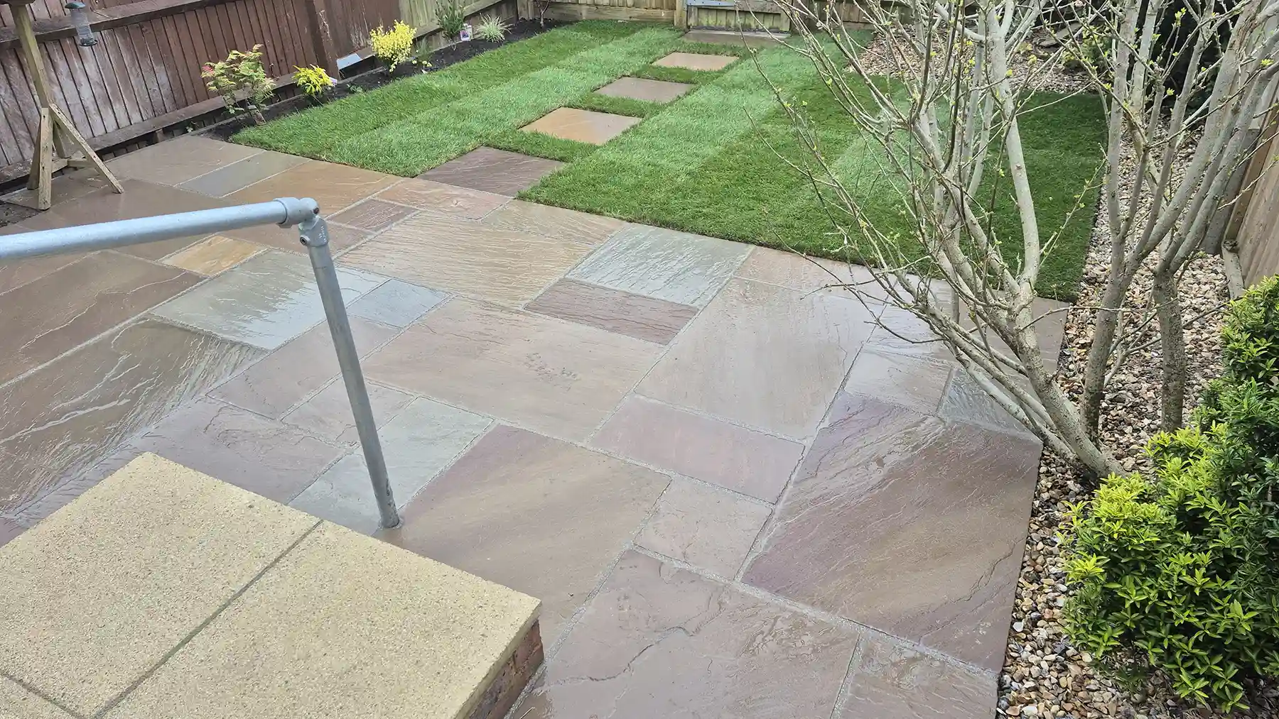 Raj blend multi-sized sandstone paving area with new lawn and flower bed with planting.