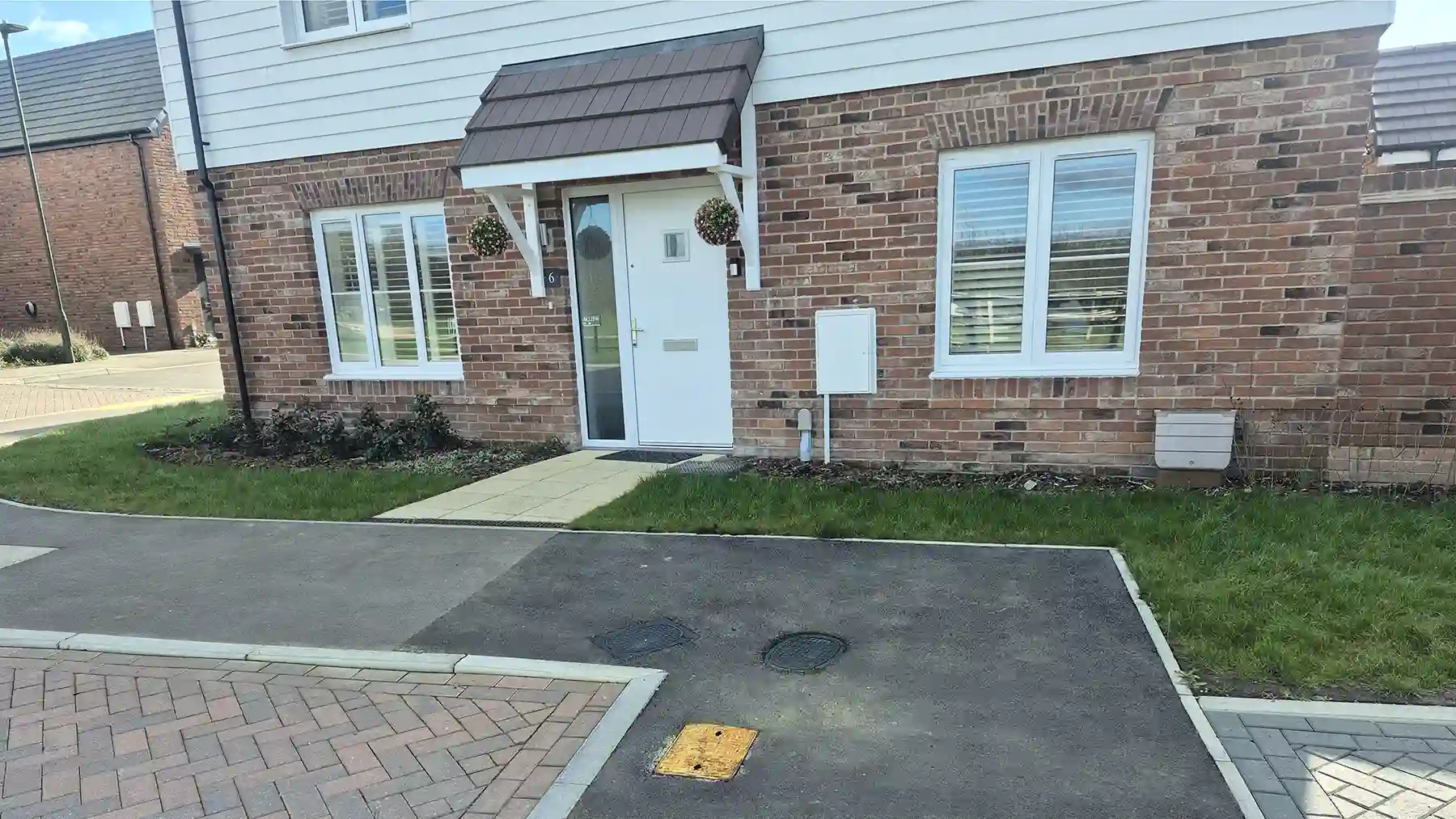 Front entrance of a modern two-story brick corner house featuring a white front door under a small canopy, white-framed windows, and a brief paved walkway.