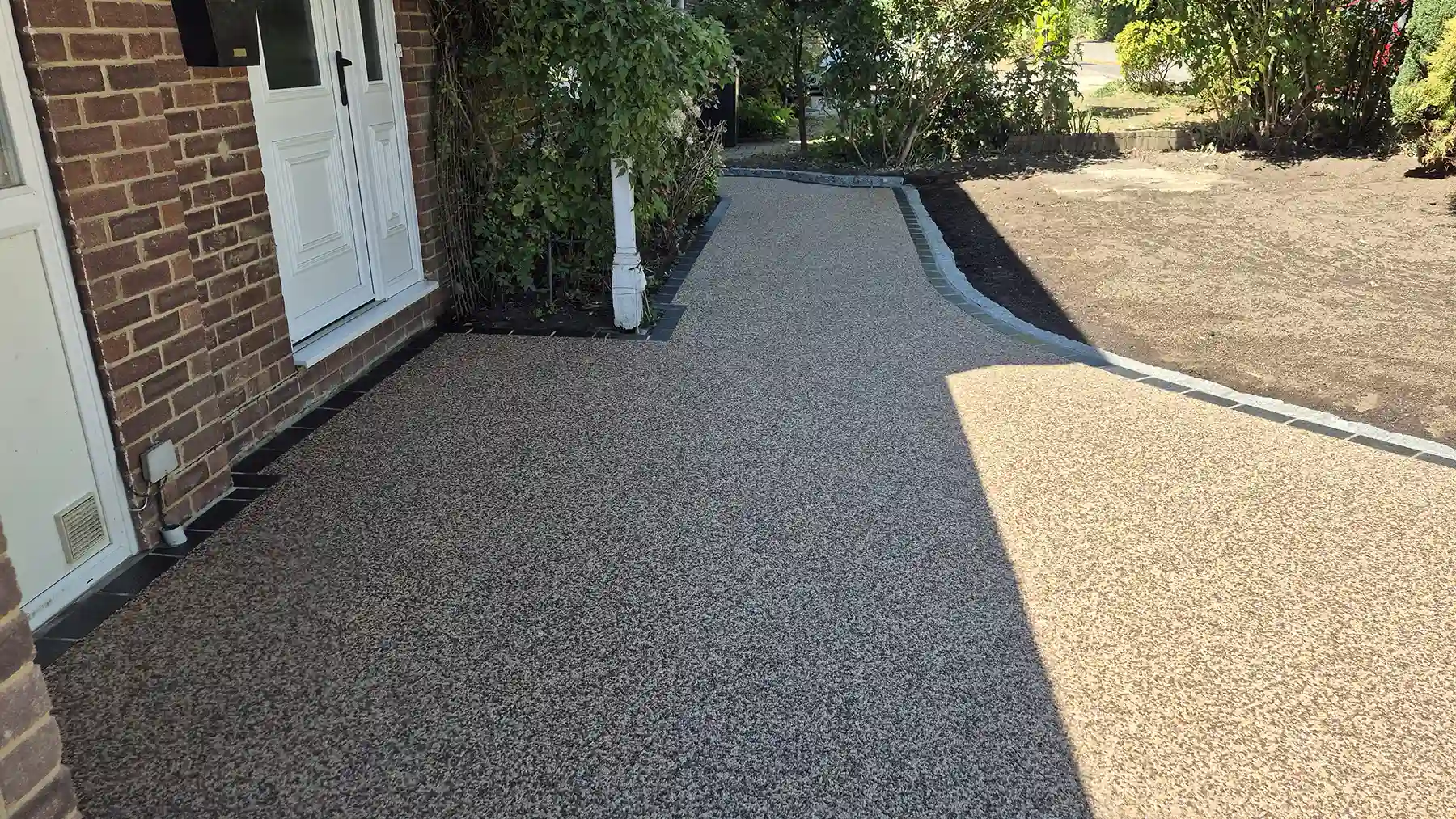 Close-up view of a freshly laid tan and grey resin-bound driveway pathway leading past a white front door and red brick house.