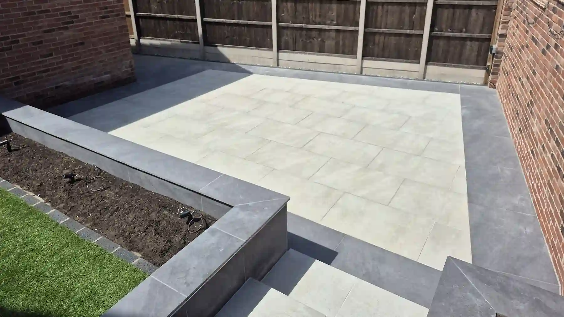 High angle view looking down onto two level porcelain paving featuring light-coloured slabs, charcoal edging slabs, built-in planter beds, and connecting steps.